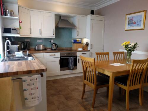 a kitchen with white cabinets and a wooden table and chairs at Sandend Cottage in Banff