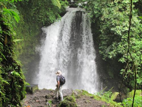 a man standing in the middle of a river with a waterfall at Arenal Observatory Lodge & Spa in Fortuna