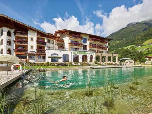 a person swimming in a pool in front of a hotel at Alpeiner - Nature Resort Tirol in Neustift im Stubaital