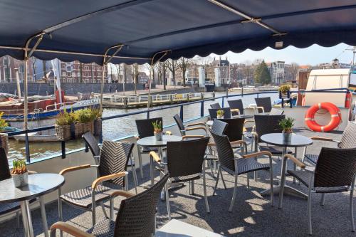 a patio with tables and chairs next to a river at Hotelboat Fleur in Amsterdam