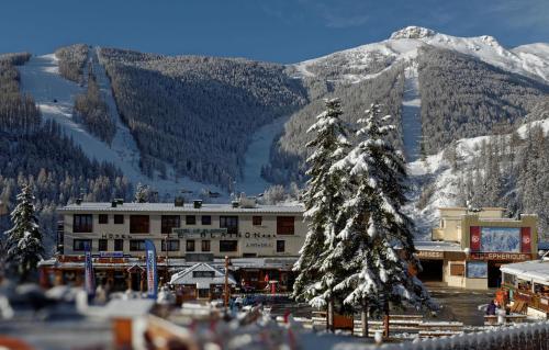 a building with a snow covered tree in front of a mountain at Hôtel Le Blainon in Auron
