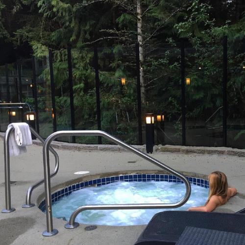 a woman sitting in a jacuzzi tub in a courtyard at Alpenglow Lodge by MVA in Whistler