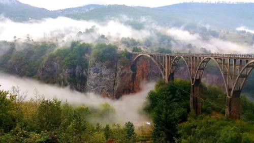 a bridge in the middle of a mountain with clouds at Holiday Home Vile Calimero in Žabljak
