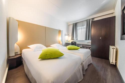 a hotel room with two beds with lime green pillows at Mandarina Hotel Luxembourg Airport in Luxembourg