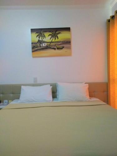 a bed with two pillows and a painting on the wall at Simas Praia Hotel in Aracaju