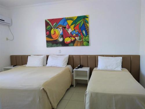 two beds in a room with a painting on the wall at Simas Praia Hotel in Aracaju