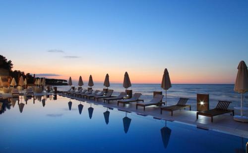 a swimming pool with chairs and umbrellas and the ocean at Atik Hotel in Unye