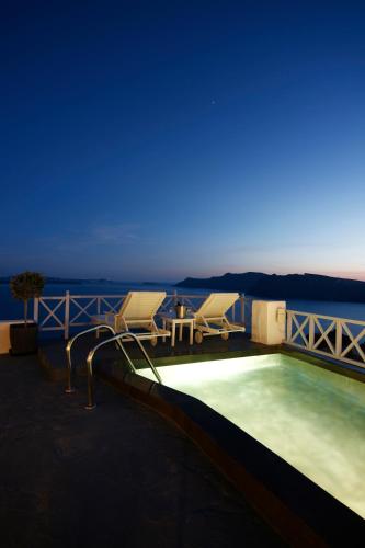 a swimming pool with two chairs and a table at Armeni Village in Oia