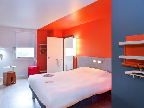 a room with a bed with an orange wall at ibis budget Saint Lô in Saint Lo