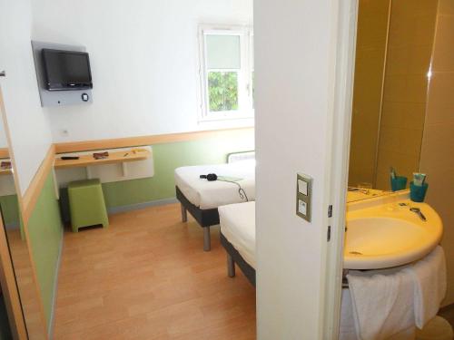 a room with two beds and a sink and a tub at ibis budget Marne la Vall&eacute;e in Saint-Thibault-des-Vignes