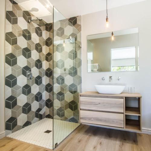 a bathroom with a shower with a sink and a mirror at Hlangana Lodge in Oudtshoorn