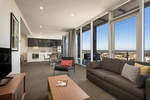 a living room with a couch and a kitchen with windows at Quest on Franklin in Adelaide