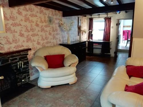 a living room with two white chairs and a fireplace at Brown Cow Cottage in Dalton in Furness