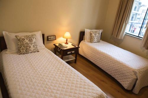 a bedroom with two beds and a table with a lamp at Kafé Hotel in Guaratinguetá