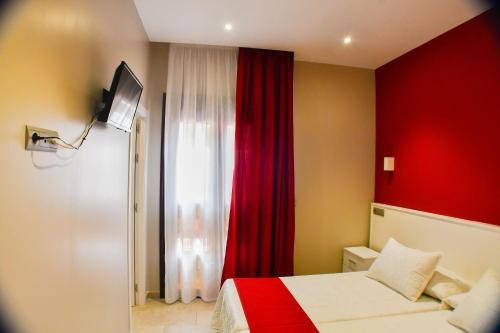ロタにあるHostal Playa Candorのベッドと赤いカーテンが備わるホテルルーム