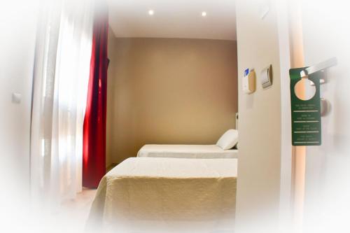 a small room with two beds and a red curtain at Hostal Playa Candor in Rota