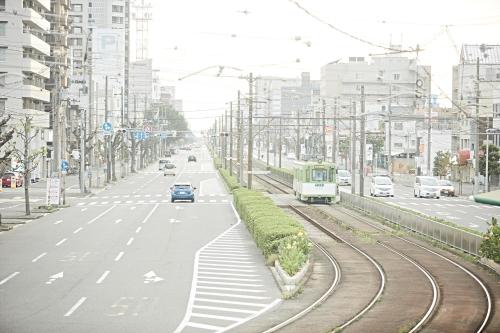 a city street with cars and a train on the road at sakainoma hotel 熊 in Sakai