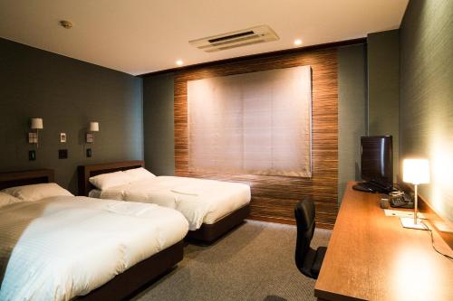 a hotel room with two beds and a desk and a window at Hotel Daiei Masuda in Masuda