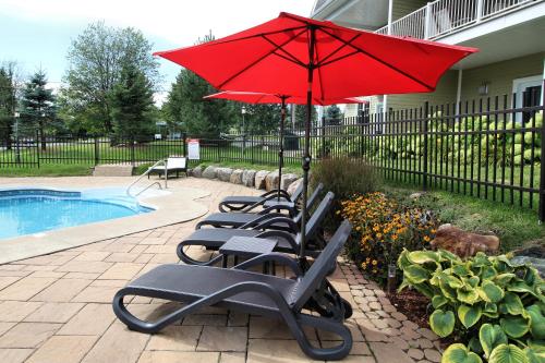 a row of chairs with a red umbrella next to a pool at Le 204 Champlain Bromont in Bromont