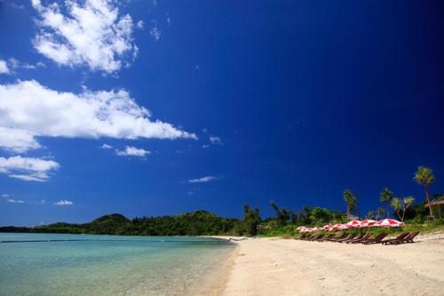 a beach with red and white umbrellas and the ocean at Ishigaki Seaside Hotel in Ishigaki Island