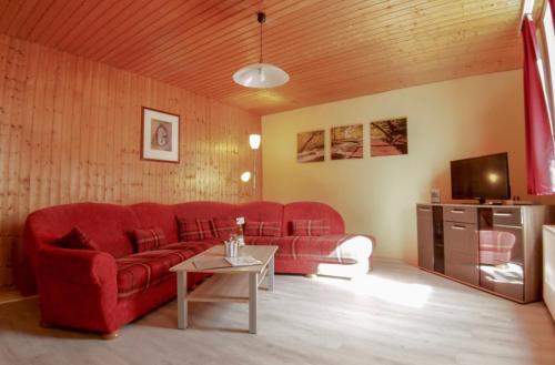 Apartments Carmen-Braunlage في برونلاغ: غرفة معيشة مع أريكة حمراء وطاولة
