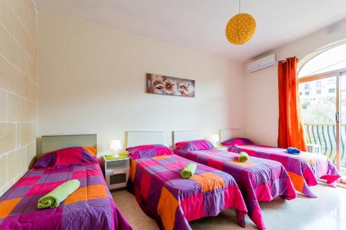three beds in a room with pink and orange at Serenity - Bellevue Gozo in Xlendi