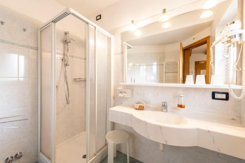 a white bathroom with a sink and a shower at Hotel Alpe in Canazei