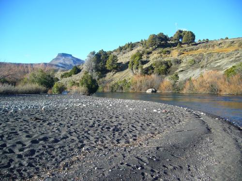 a river with a rocky shore next to a mountain at Cabañas Boca del Chimehuín in Junín de los Andes