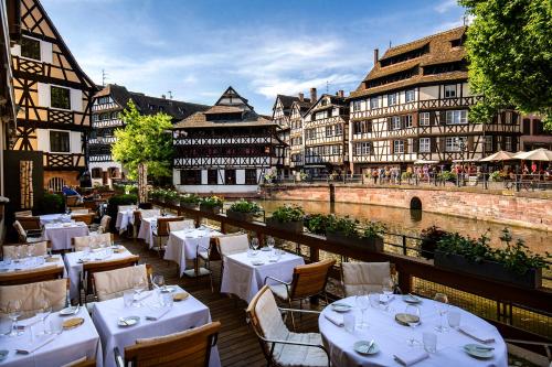 een restaurant met witte tafels en stoelen naast een rivier bij Hotel & Spa REGENT PETITE FRANCE in Straatsburg