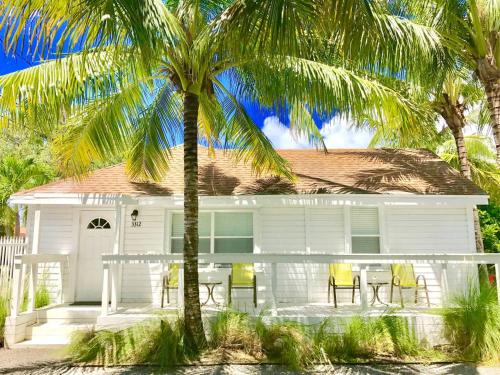 a white house with yellow chairs and a palm tree at Grove Bay Bungalow - 2/2 Gated Cottage-Walk to Bay in Miami