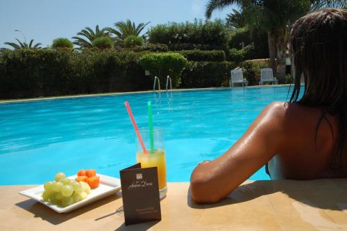 a woman sitting at a table with a plate of fruit and a drink at Andrea Doria Hotel in Marina di Ragusa