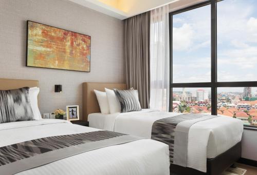two beds in a hotel room with a large window at Somerset Norodom Phnom Penh in Phnom Penh