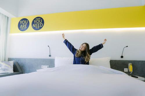 a woman is raising her arms above a bed at YELLO Hotel Paskal Bandung in Bandung