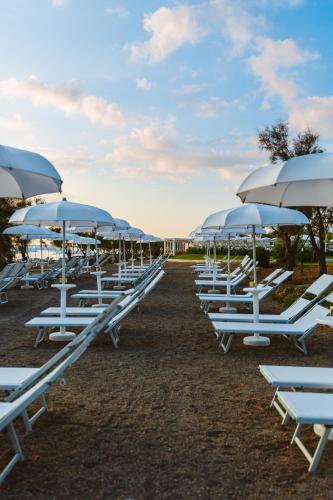 a row of white lounge chairs and umbrellas at Torre Cintola Greenblu Sea Emotions in Monopoli