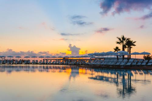 a resort with chairs and umbrellas on the water at sunset at Torre Cintola Greenblu Sea Emotions in Monopoli