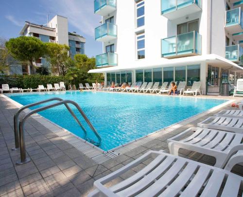ein Pool mit weißen Stühlen und ein Gebäude in der Unterkunft Hotel Katja in Bibione