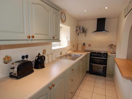 a kitchen with white cabinets and a sink and a stove at Acorn Cottage in Bruton