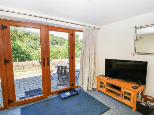 a living room with a television and a sliding glass door at Hove Wood View in Hebden Bridge