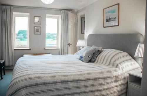 a bedroom with a large bed with two windows at Acorn Cottage in Bruton