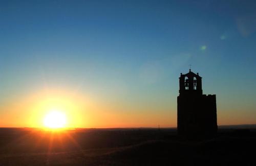 a clock tower with the sunset in the background at Hotel Rural El Adarve in Ayllón