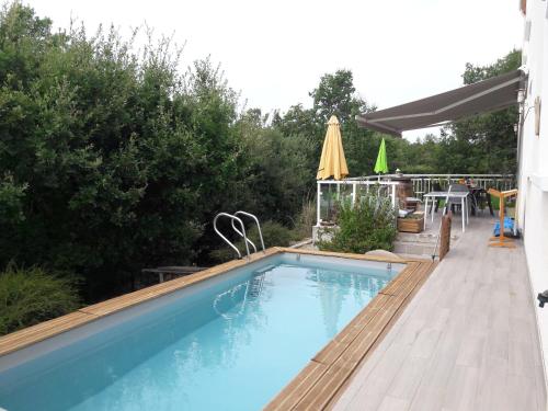 a swimming pool with a deck and a table and umbrella at La maison familiale in Lagarrigue