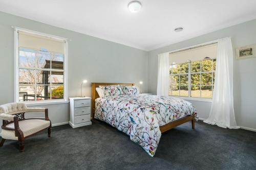 a bedroom with a bed and a chair and windows at A House With A View, Molong. NSW in Molong