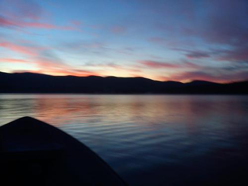 a sunset on a lake with a boat in the water at Stora Björnstugan in Laisvall