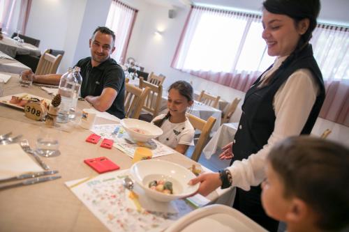 a woman serving food to children at a table at Hotel Luna Bianca Folgaria in Folgaria