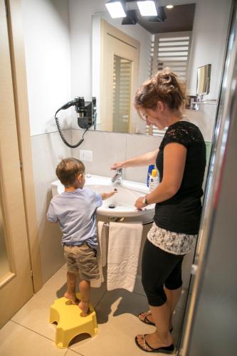 a woman and a young boy standing in a bathroom sink at Hotel Luna Bianca Folgaria in Folgaria