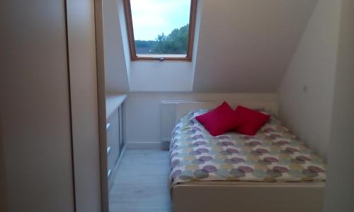 ein kleines Schlafzimmer mit einem Bett mit zwei roten Kissen in der Unterkunft Kama Apartament Kamień Pomorski in Cammin in Pommern