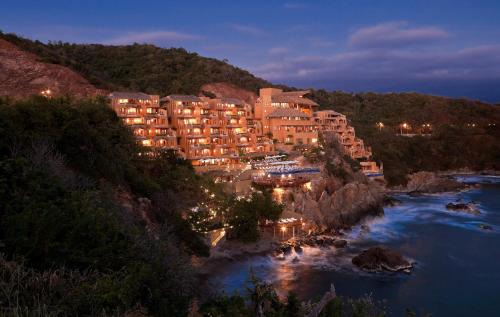 a hotel on a hill next to a river at night at Cala de Mar Resort & Spa Ixtapa in Ixtapa
