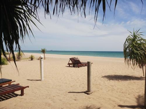 a beach with chairs and a bench on the sand at Villa Nilaveli Cabana in Nilaveli