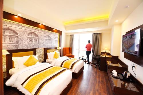 a hotel room with two beds and a man looking out the window at Regenta Central Srinagar, Rajbagh in Srinagar
