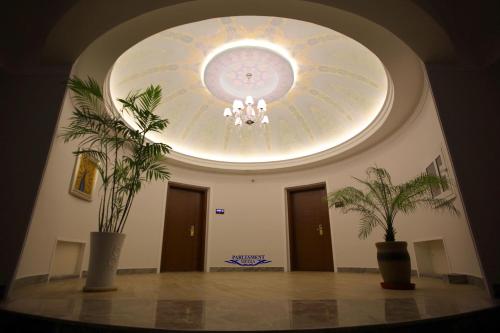 a room with a ceiling with a chandelier and two plants at Parliament Palace Hotel in Khujand
